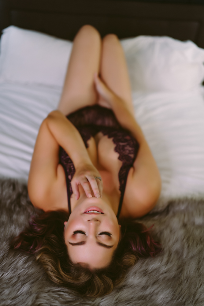 A woman lays on a bed in preparation for a boudoir photo shoot.