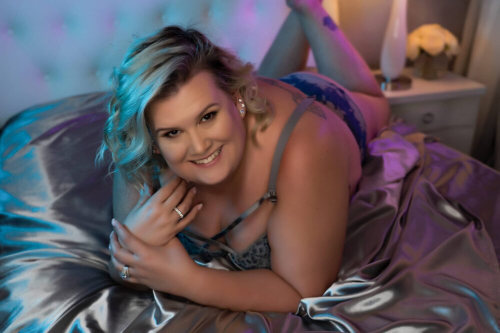 woman posing on boudoir studio bed with silver satin sheets