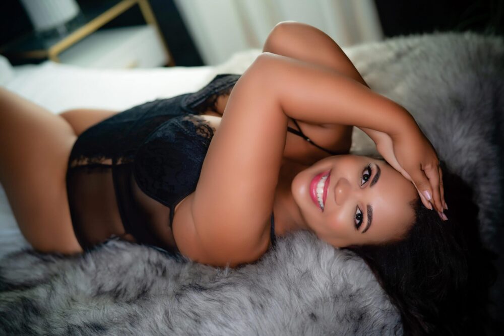 A beautiful woman in black lingeries laying on a furry bed.
