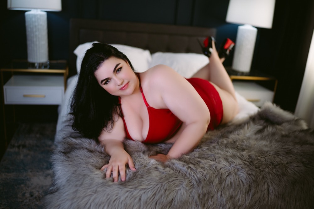 A woman in a red dress lounging on a bed, captured through Northern Virginia Boudoir Photography.