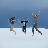 Three people jumping in the air on a sandy beach.