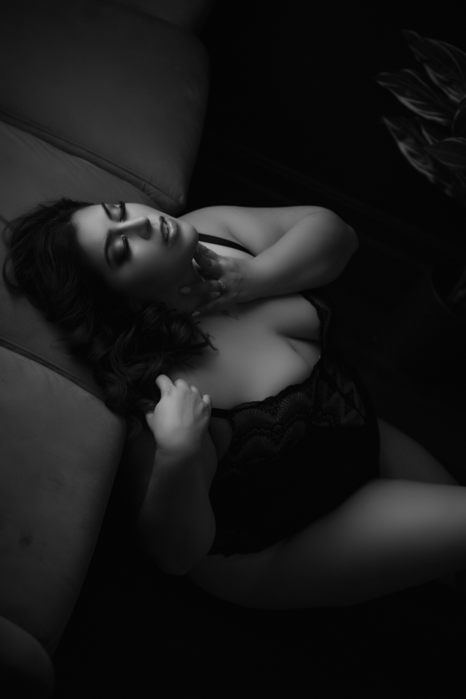 A black and white photo of a woman reclining on a couch, captured by Northern Virginia Boudoir Photography.
