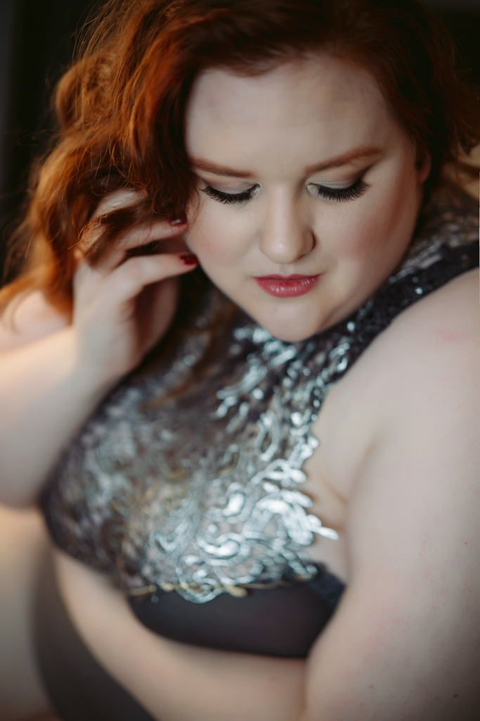 close up of a beautiful woman touching her face looking down wearing a silver bodysuit in boudoir studio