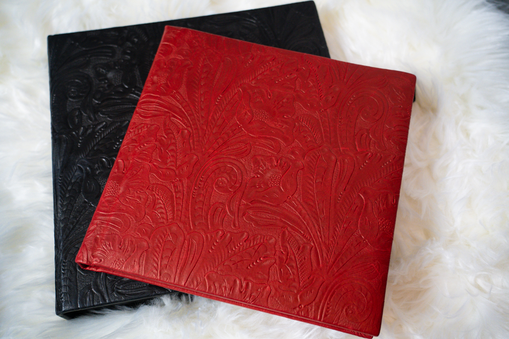 Two red and black leather notebooks are placed on a white fur rug by Kellie Frye Photography.