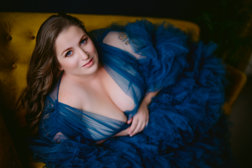 A woman in a blue tulle dress poses on a yellow couch for her Northern Virginia boudoir photography session.