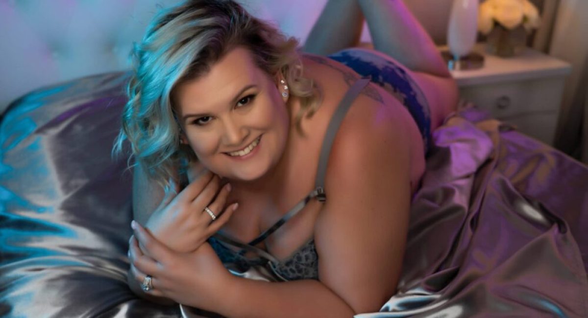 woman posing on boudoir studio bed with silver satin sheets